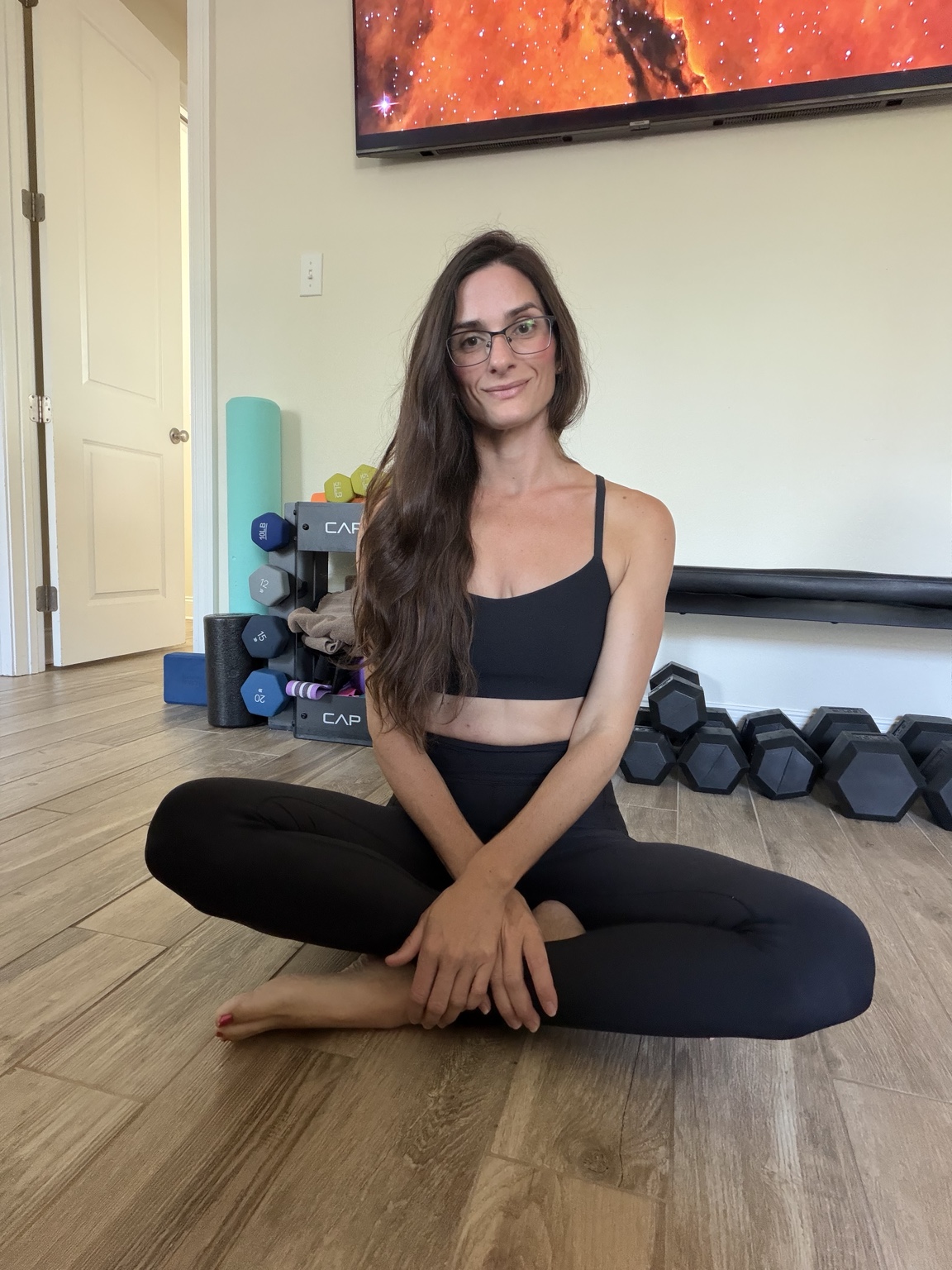Ashley seated on the floor beside her home workout equipment