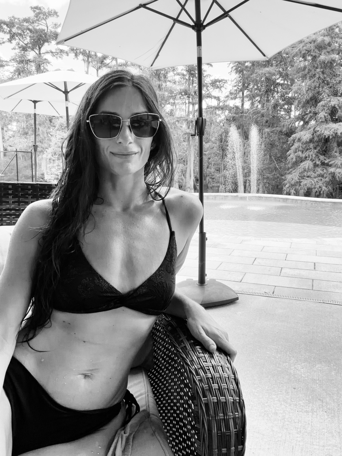 Black-and-white portrait of Ashley in sunglasses beside the pool